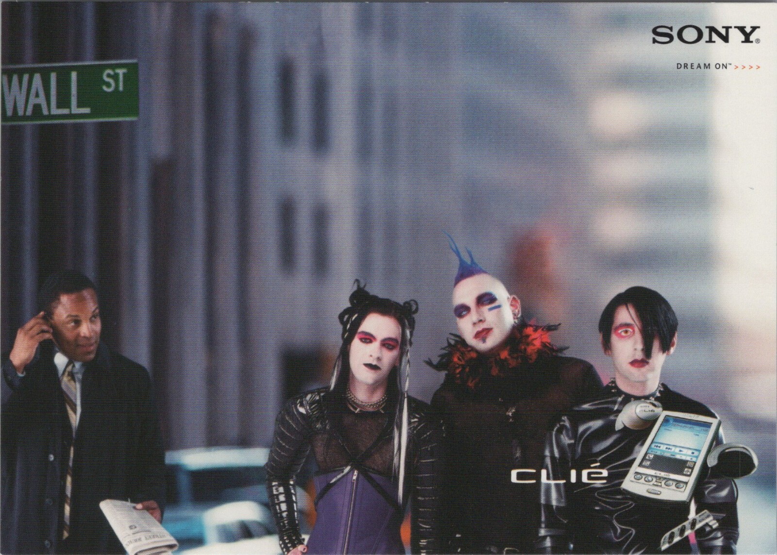 Wall Street. A businessperson on their cellphone looks incredulous at three people composited into the scene who are done up in mallgoth style: white pancake foundation, heavy eye makeup, pleather bondage gear, cyberfalls, a mohawk, etc. A Sony Clié with mp3 attachment is superimposed in the corner over one of them. Wall Street. A businessperson on their cellphone looks incredulous at three people composited into the scene who are done up in mallgoth style: white pancake foundation, heavy eye makeup, pleather bondage gear, cyberfalls, a mohawk, etc. A Sony Clié with mp3 attachment is superimposed in the corner over one of them.